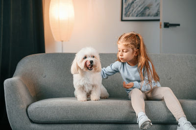 Portrait of young woman with dog sitting on sofa at home