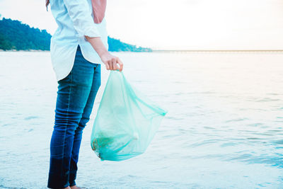 Low section of woman holding plastic at beach