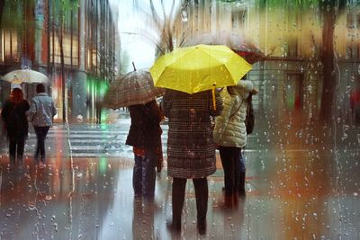 Rear view of man with umbrella walking on puddle