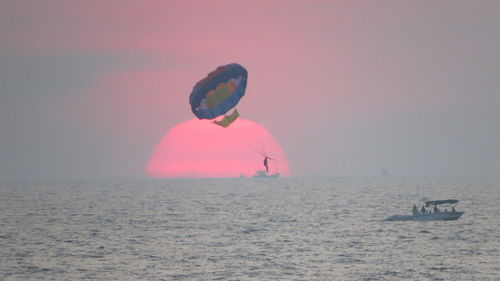 Man parasailing over sea against sky during sunset