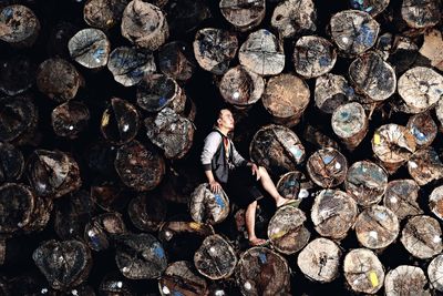 Man looking away while sitting on woodpile