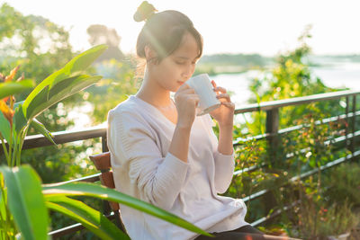 Young woman looking away while standing against plants