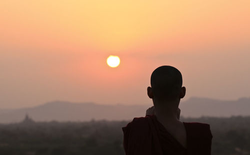 Rear view of monk against orange sky during sunset