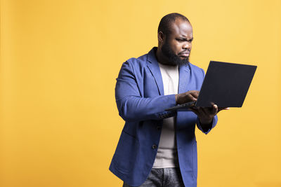 Midsection of businessman using digital tablet while standing against yellow background