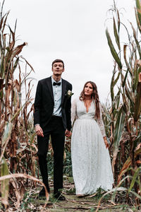 Newlywed couple standing amidst plants against clear sky