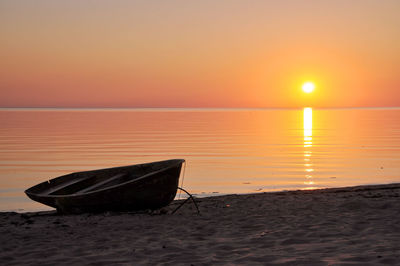 Boat moored at beach against orange sky during sunset
