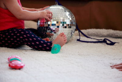 Low section of girl sitting by disco ball on rug