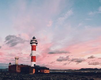 Lighthouse by sea against sky during sunset