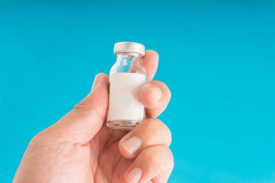 Close-up of hand holding bottle against blue background