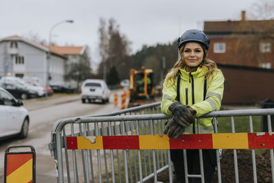 Portrait of female road worker leaning against traffic barrier
