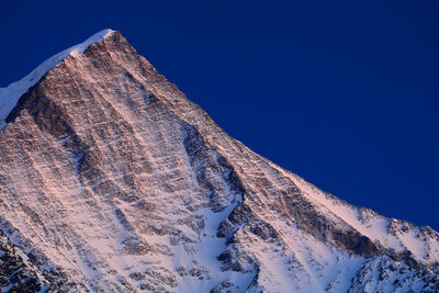 Low angle view of rocky mountains against clear blue sky