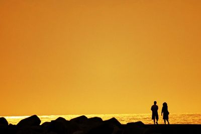 Silhouette people standing on rock by sea against clear sky during sunset