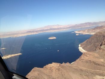 Aerial view of sea and mountains against blue sky