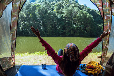 Rear view of woman sitting on mat by lake