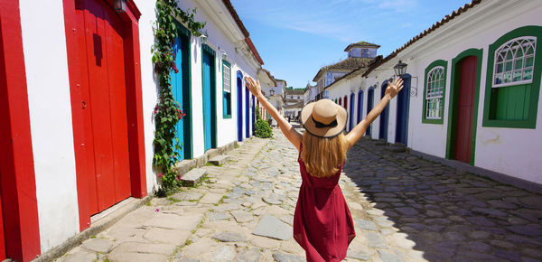 Beautiful young woman with raised arms walking in colorful historic town of paraty