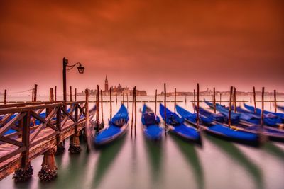 Boats moored in canal against sky during sunset