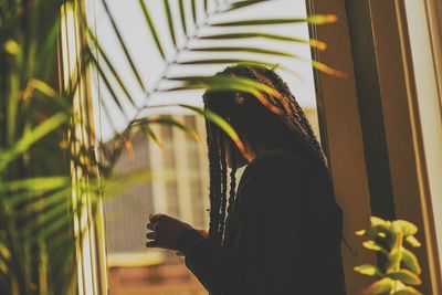 Side view of man with braided hair standing by window