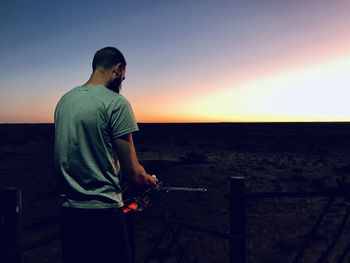 Man standing by sea against sky during sunset