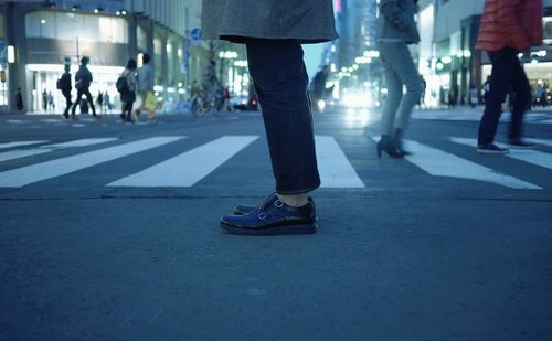 Low section of woman standing by crosswalk on street at dusk in city