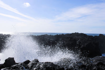 Sea waves splashing on rocks against sky