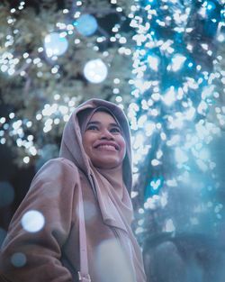 Low angle view of smiling woman in traditional clothing standing against tree