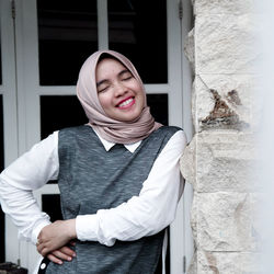 Portrait of smiling young woman standing against wall