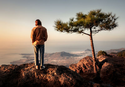 Rear view of man standing on rock against sky