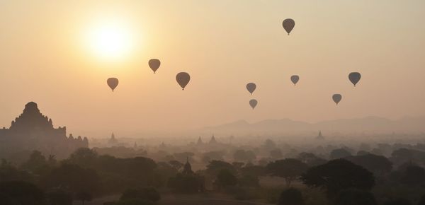 Hot air balloons flying over historic temples against sky at morning