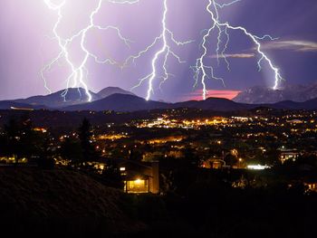 Lightning over illuminated cityscape against sky at night