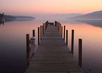 Wooden pier over lake against sky during sunset