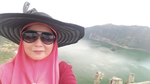 Woman wearing hijab with sunglasses and hat against lake