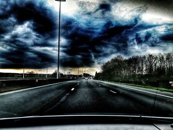 Road passing through highway against cloudy sky