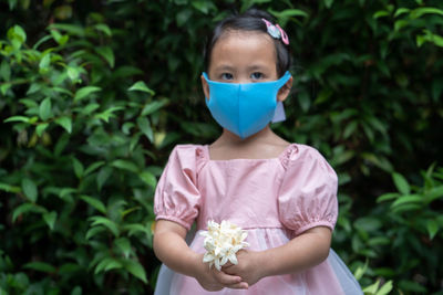 Portrait of cute girl holding flower against plants