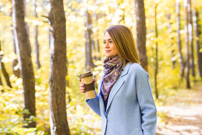 Young woman standing by tree in forest during autumn