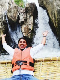 Portrait of smiling young man siting in basket against waterfall