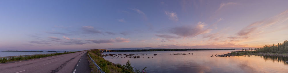 Panoramic shot of road by river against sky during sunset