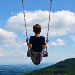 Rear view of boy on swing against cloudy sky