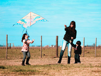 Woman flying kite with children on field against blue sky