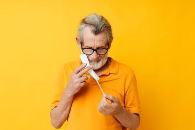 Portrait of young woman drinking coffee against yellow background