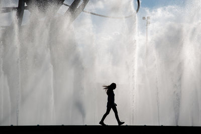 Side view of silhouette woman walking on footpath by fountain