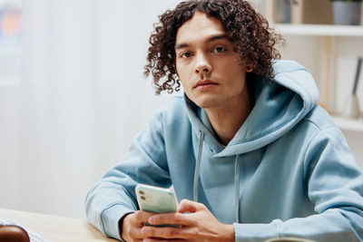 Portrait of young man holding mobile phone at home