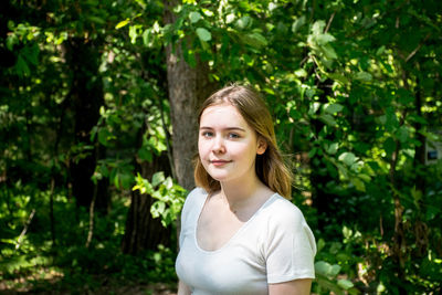 Portrait of young woman standing against trees