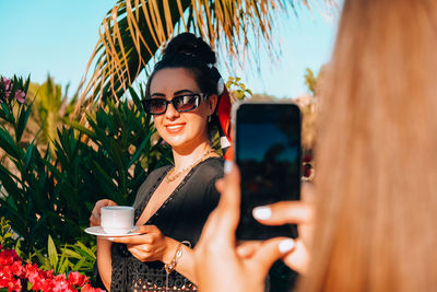 Portrait of smiling young woman wearing sunglasses while standing against sky