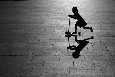 Silhouette of girl riding push scooter on pavement
