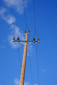 Low angle view of electricity pylon against blue sky