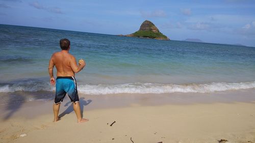 Rear view of shirtless man standing at beach