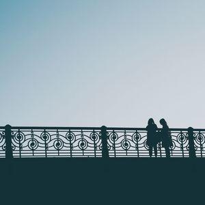 Silhouette people standing on railing against clear sky