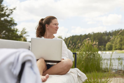 Woman using laptop on garden bench barefoot