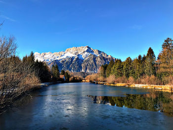 Scenic view of lake by snowcapped mountains against clear blue sky