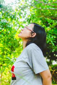 Side view of young woman standing against plants